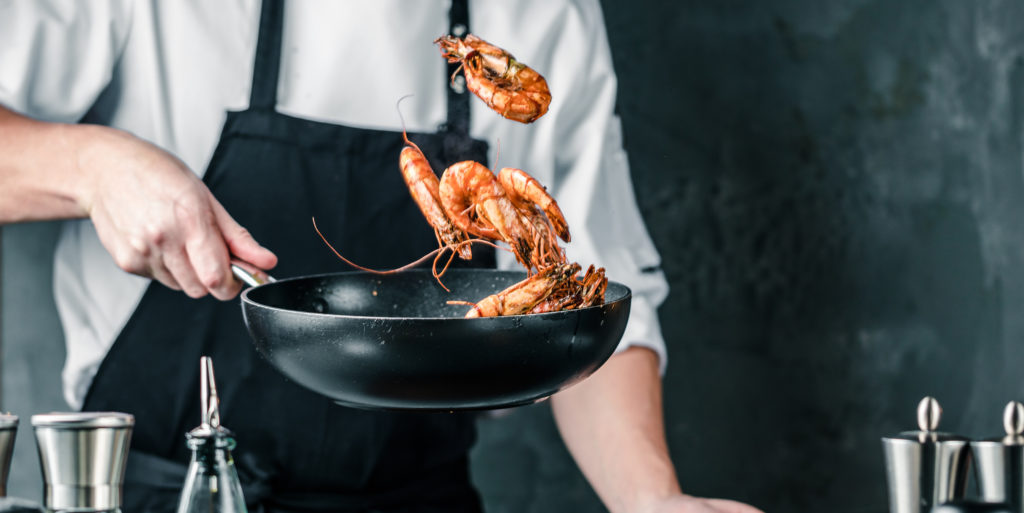 Le chef fait sauter des crevettes dans une poêle