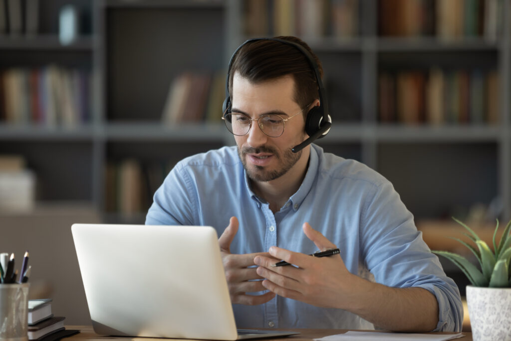 A man wearing a headset and talking on a virtual call through the computer